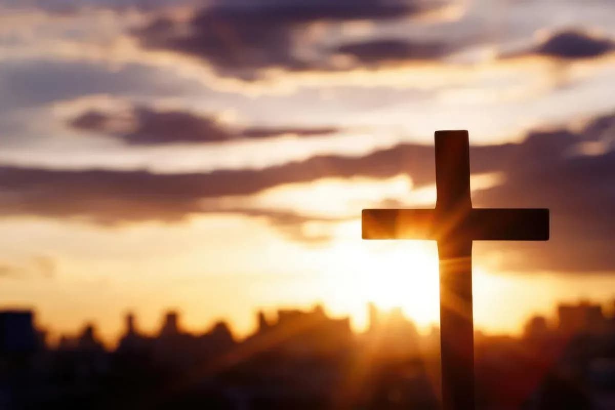 Wooden cross silhouetted against a glowing sunset.