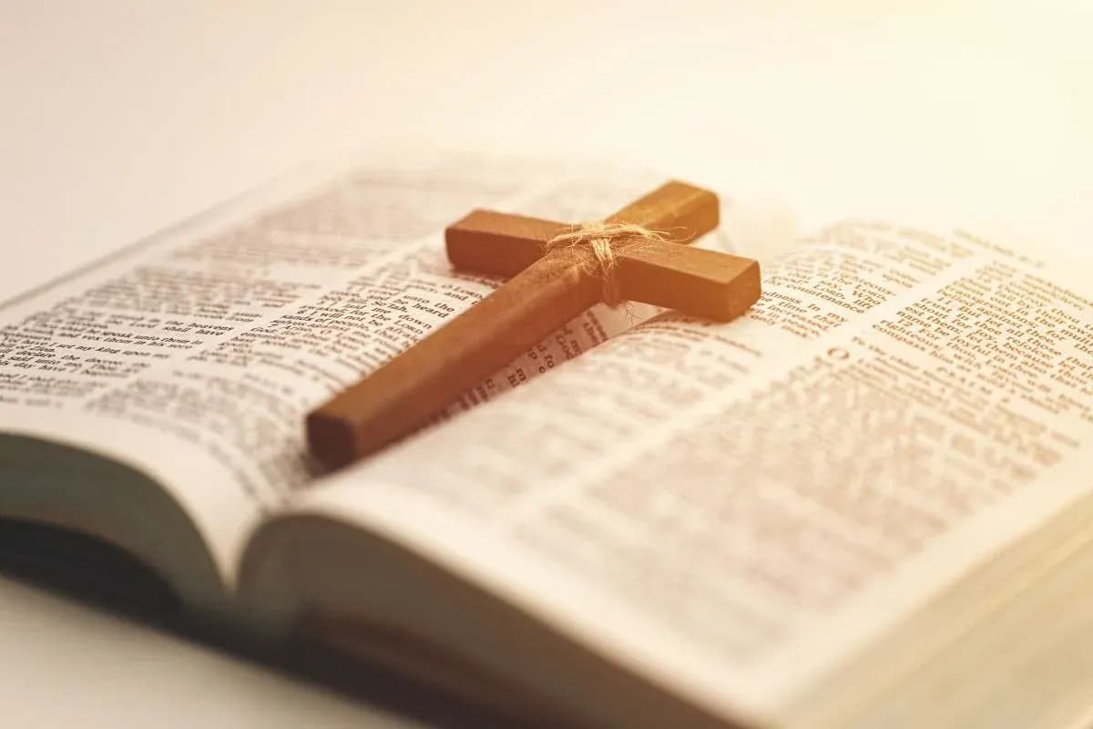 Wooden cross resting on the pages of an open Bible.