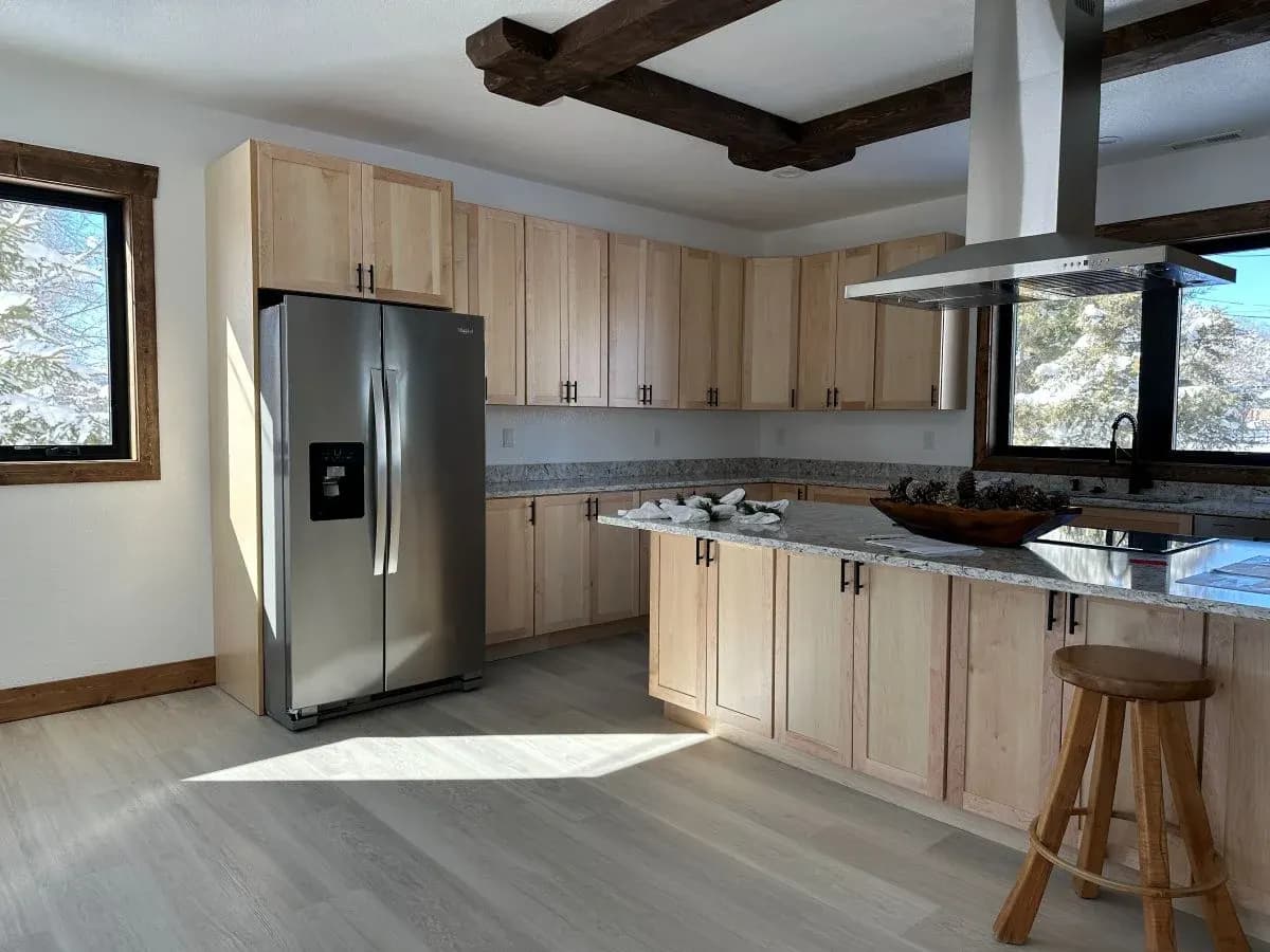 Custom kitchen with light wood cabinetry, large island, exposed wood beams, and stainless steel appliances in Buffalo, Wyoming