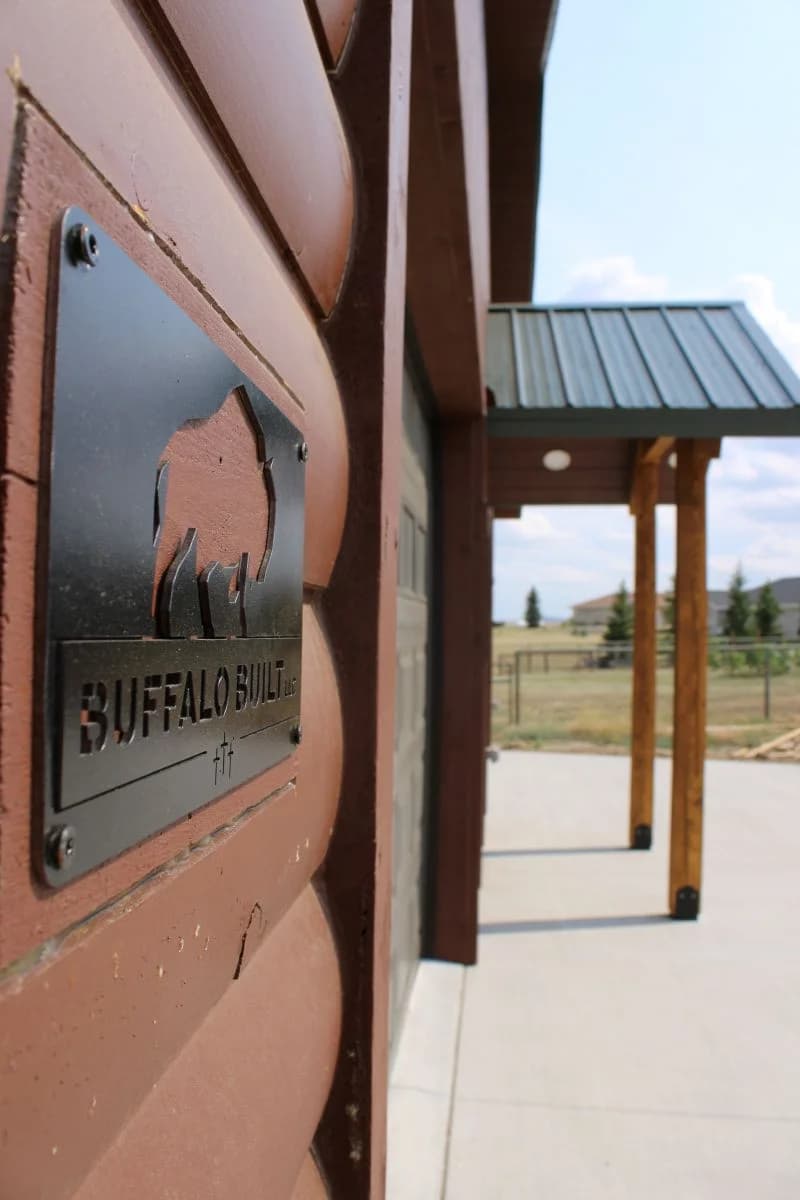 Custom metal Buffalo Built LLC company plaque mounted on log-lap siding of a completed commercial build in Wyoming.